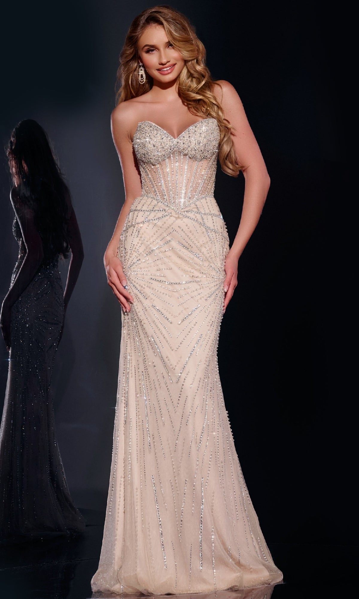 A woman smiles against a dark background wearing the Jovani 42206, a long strapless prom dress with sparkly embellishments and a sheer corset bodice.